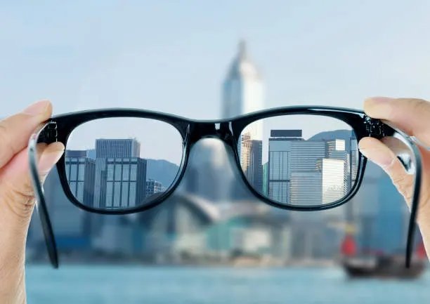 Hands holding eyeglasses up to a city skyline, the view sharp through the lenses